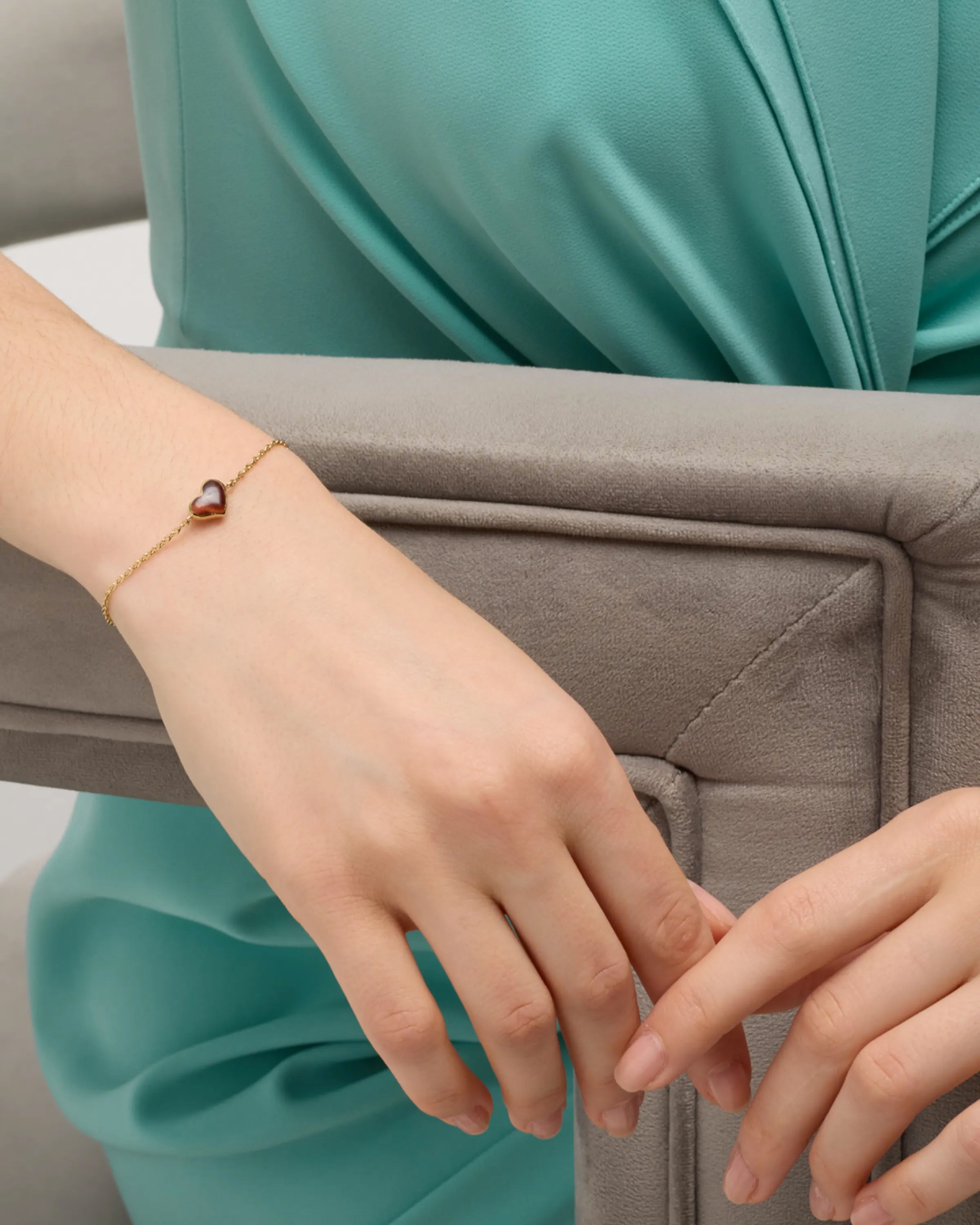 Woman in teal dress wearing rose gold vermeil red tiger eye heart chain bracelet at wrist showing burgundy-red tiger eye heart station on rose gold cable chain by Jan Leslie