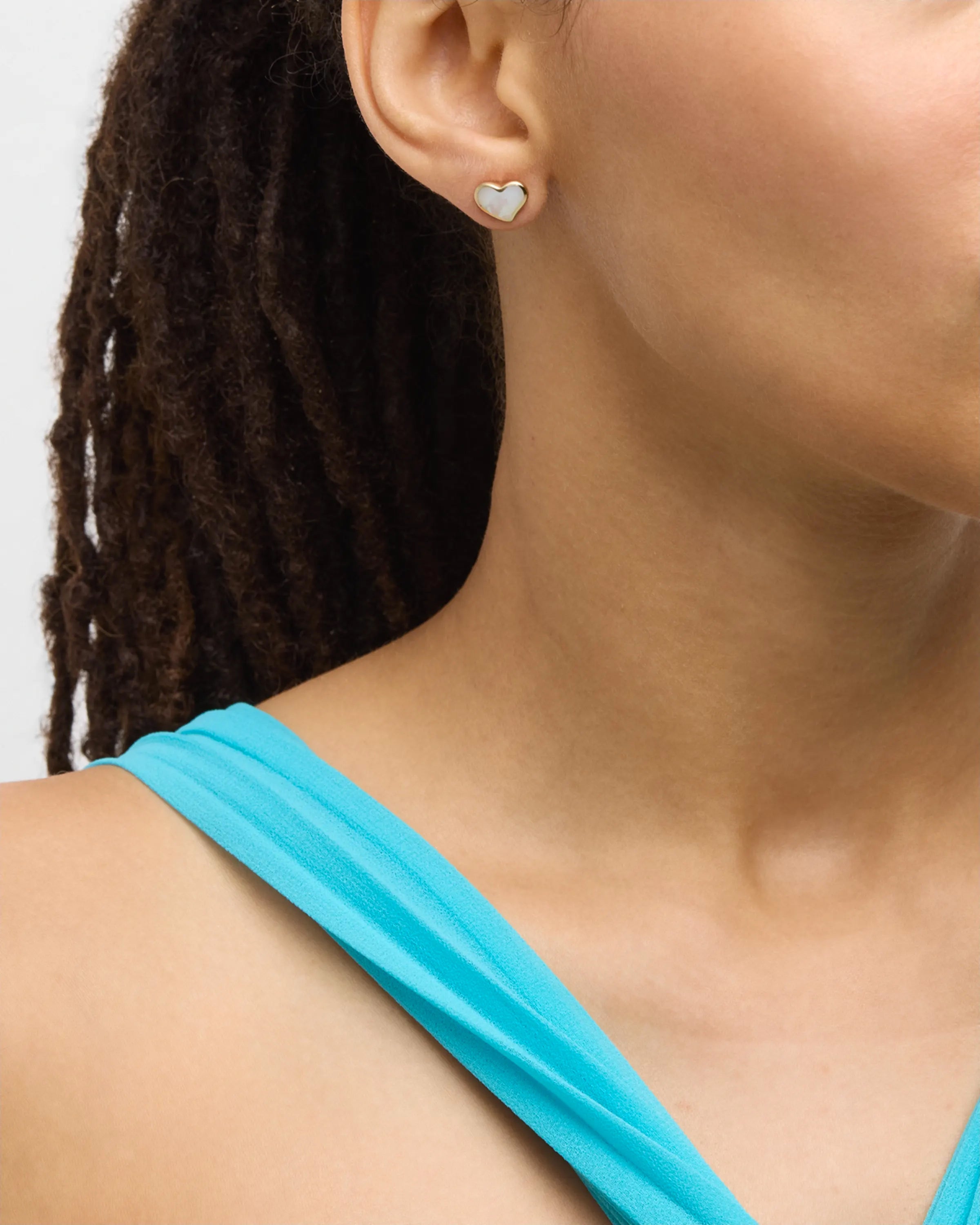 Model in teal dress wearing white mother-of-pearl heart inlay gold stud earring, ear profile view — Jan Leslie