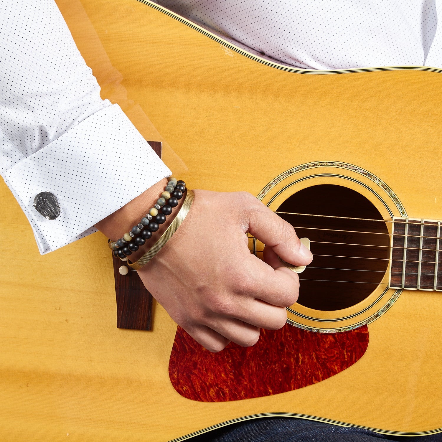 Close up of male models wrist donning Delta Trilobite Fossil Sterling Silver Cufflinks on a patterned white cuffed shirt.