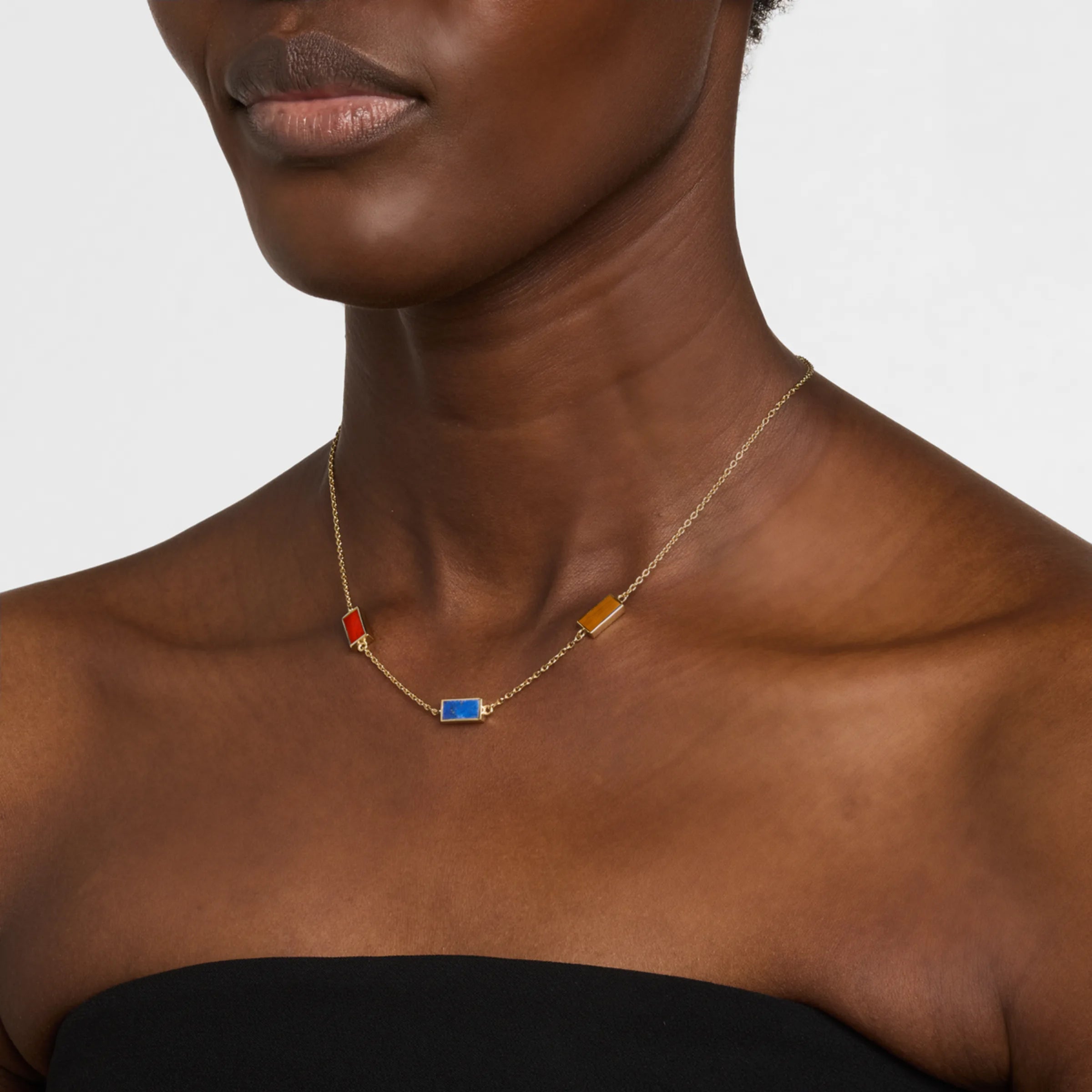 Woman in black strapless top wearing a gold cable chain station necklace with mixed carnelian, lapis lazuli, and tiger's eye rectangular gemstone pendants.