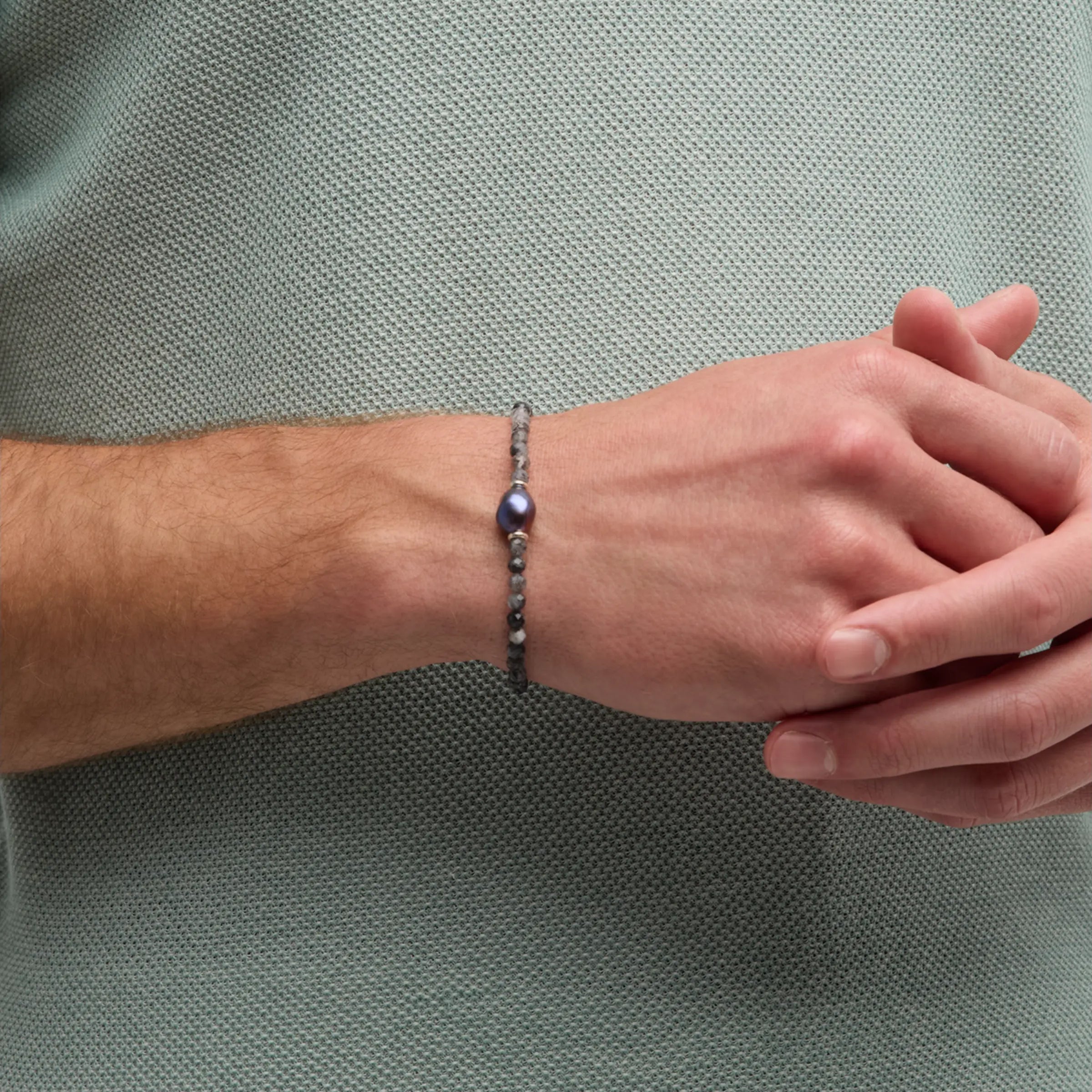 Man wearing black tourmalinated quartz and baroque peacock pearl bracelet on wrist with sage green polo shirt hands clasped by Jan Leslie
