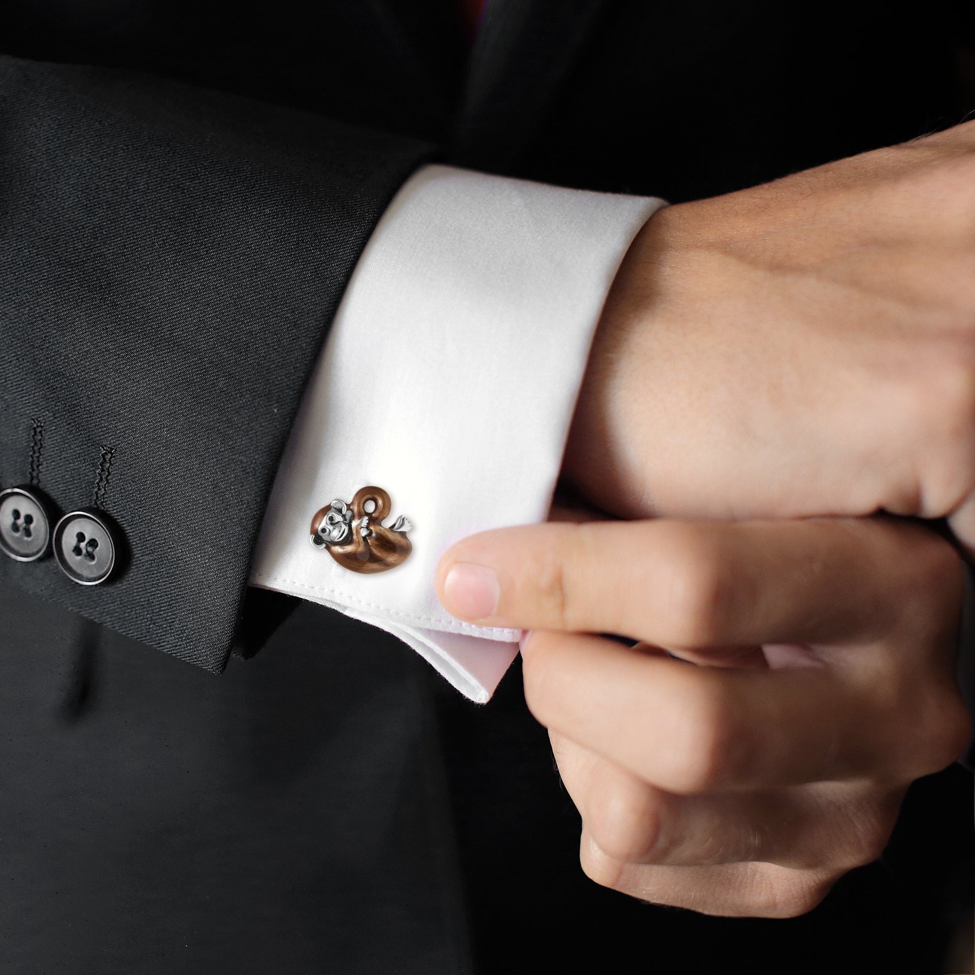 Man fastening sterling silver brown enamel monkey cufflinks on white French cuff with black tuxedo jacket, luxury novelty men's fine jewelry lifestyle.