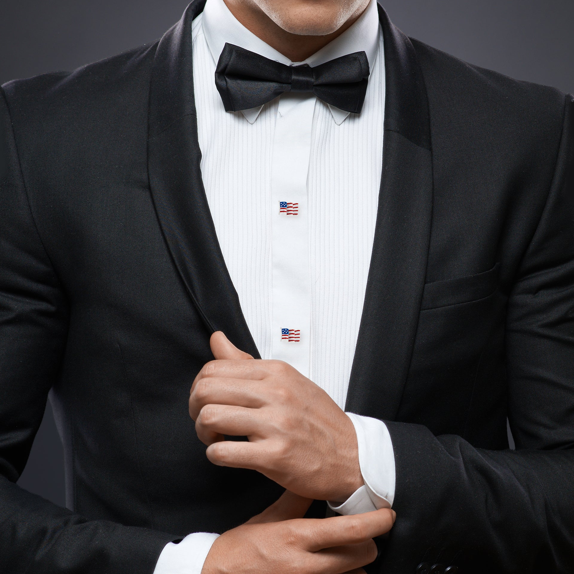 Man in black tuxedo with bow tie wearing American flag enamel tuxedo studs down the placket of a white pleated dress shirt.