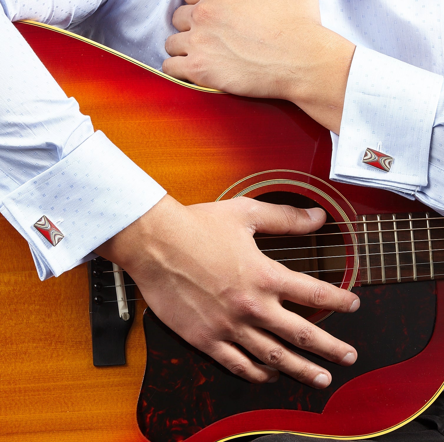 Close up of Corvette Fordite Sterling Silver Cufflinks in red on a light blue patterned cuffed shirt.
