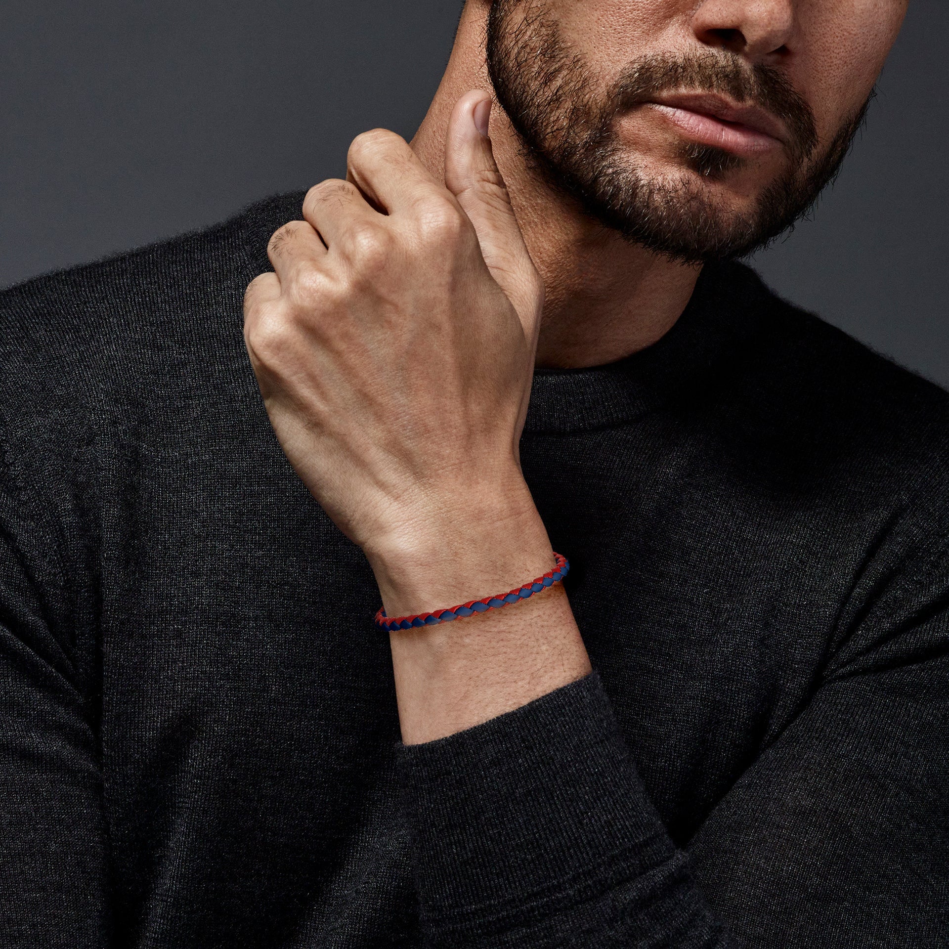 Red and blue two-tone braided leather bracelet with magnetic clasp worn on man's wrist with dark grey sweater