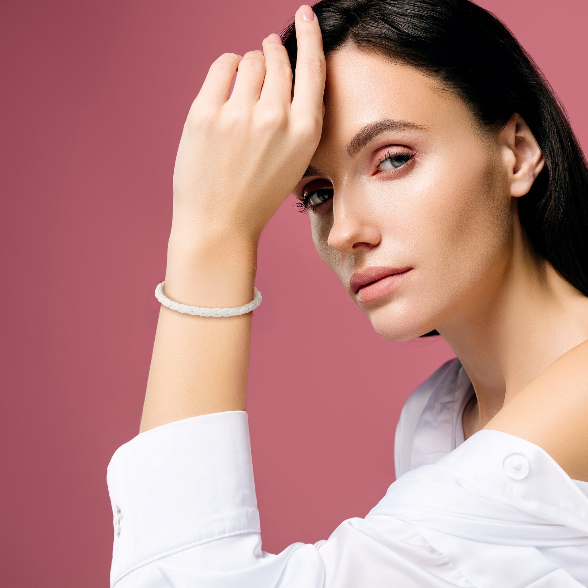 Model wearing white braided leather bracelet with gold magnetic clasp on wrist with white top against pink background by Jan Leslie.