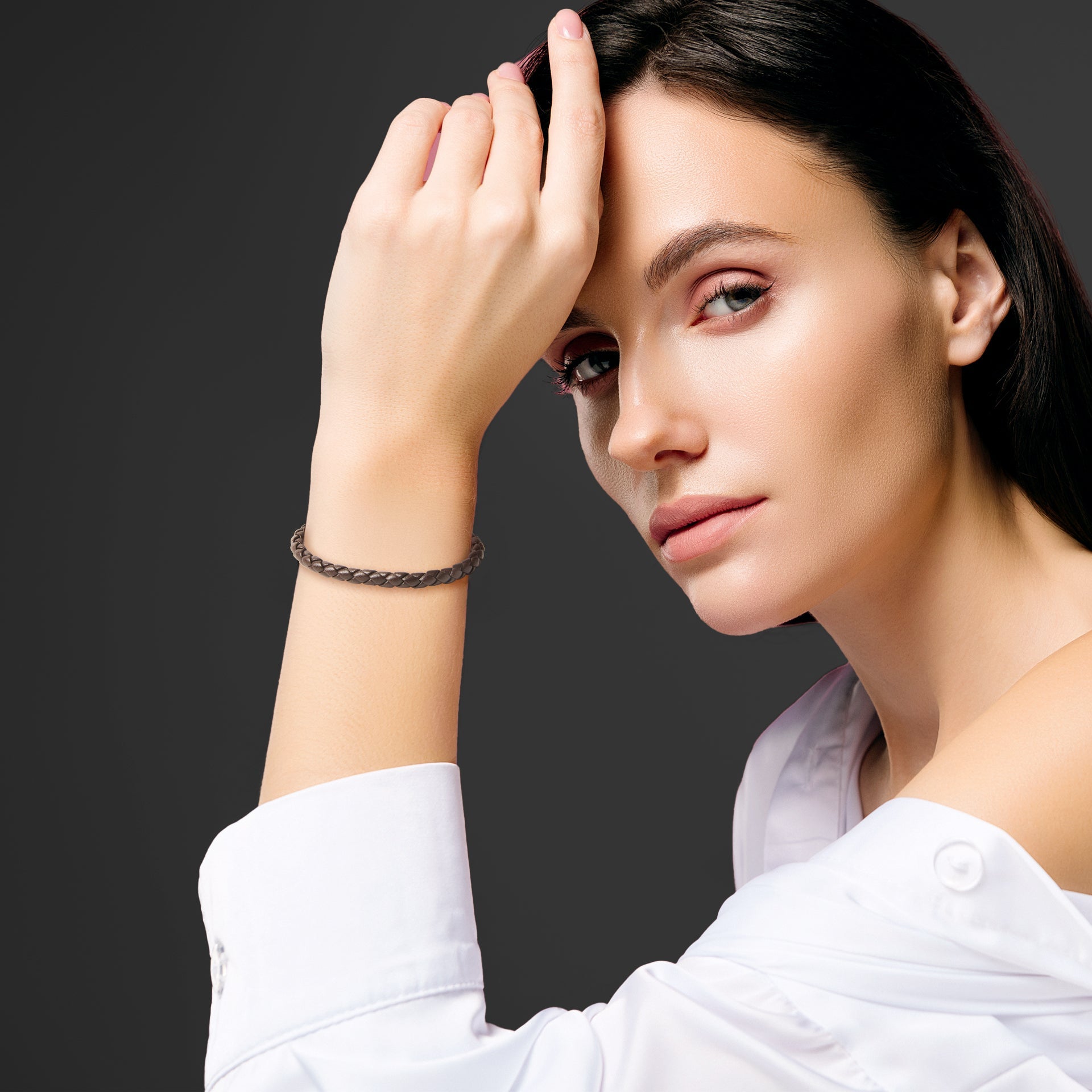 Woman in white off-shoulder top wearing a dark brown braided leather bracelet with gold magnetic clasp.