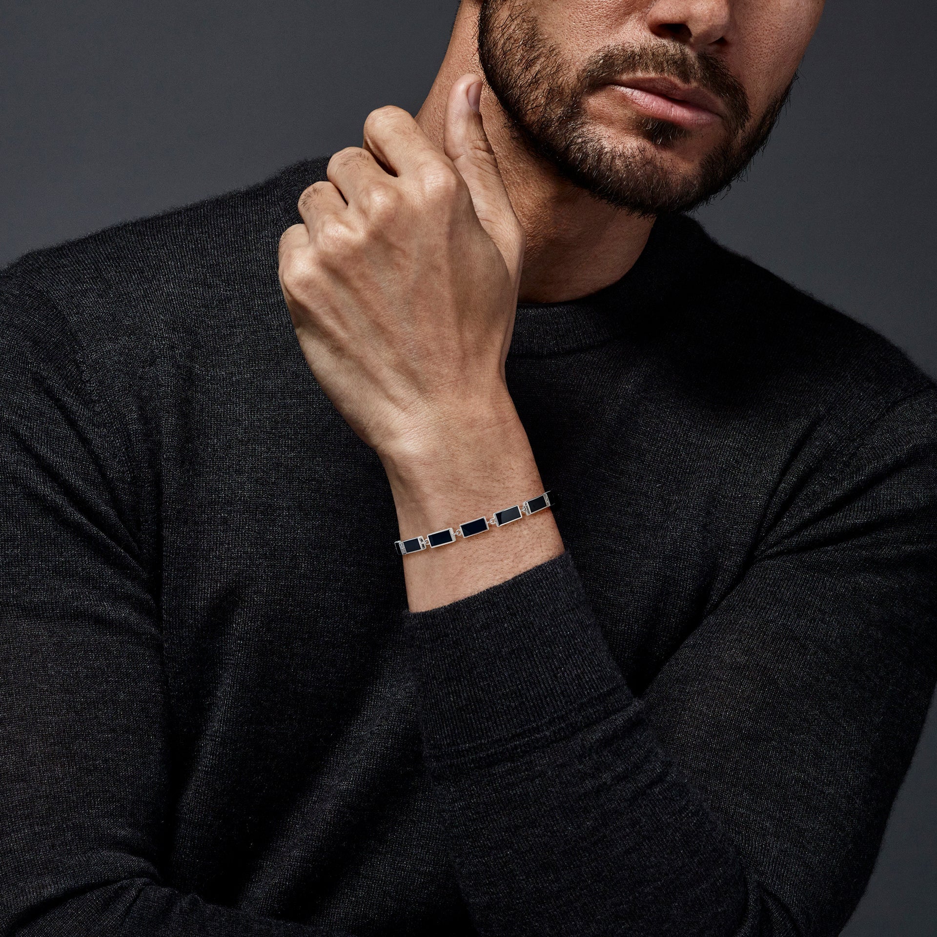  Man in charcoal turtleneck wearing sterling silver black onyx rectangular station tennis bracelet at wrist hand raised to chin editorial view by Jan Leslie