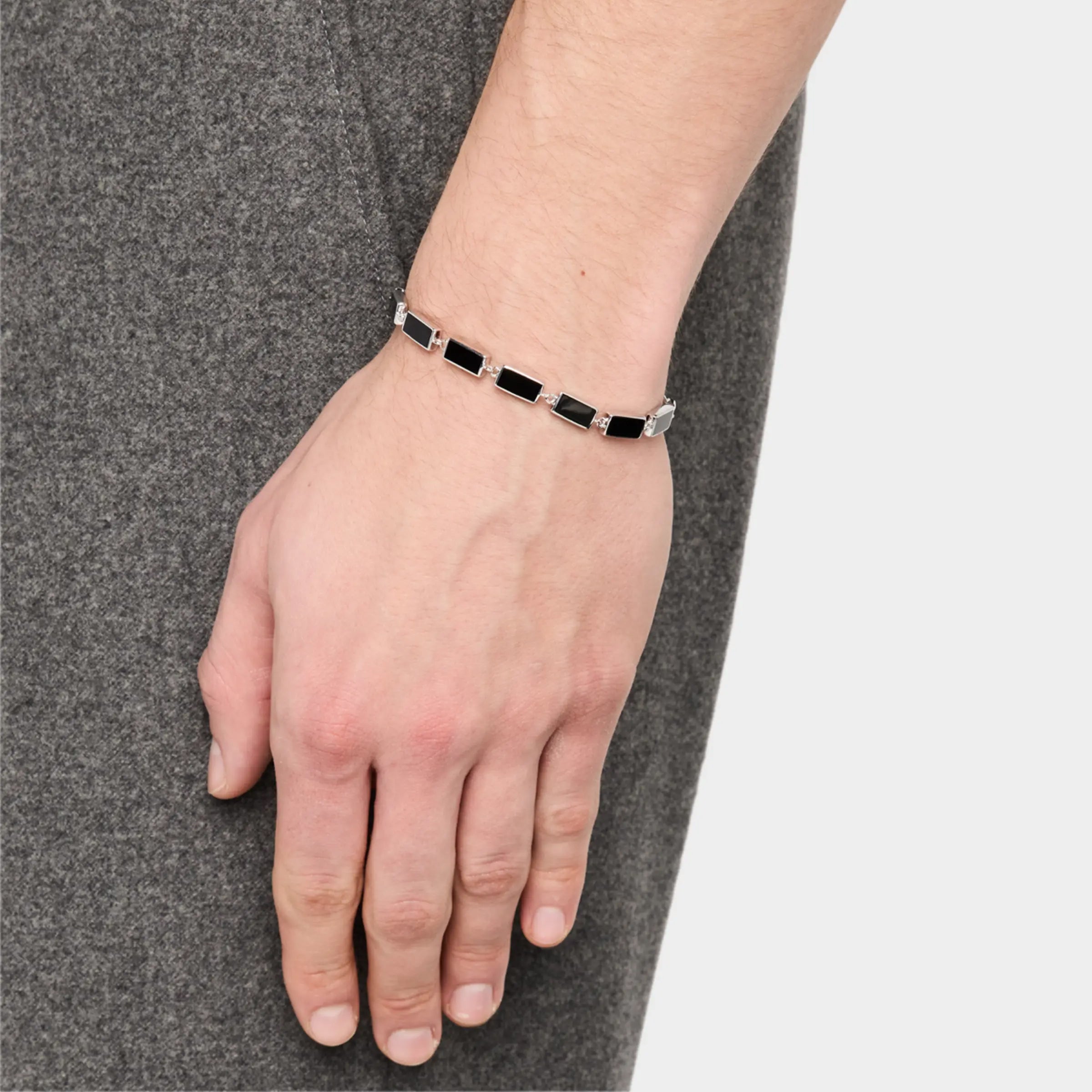 Man in grey knit wearing sterling silver black onyx rectangular station tennis bracelet at wrist showing continuous black onyx stone face by Jan Leslie