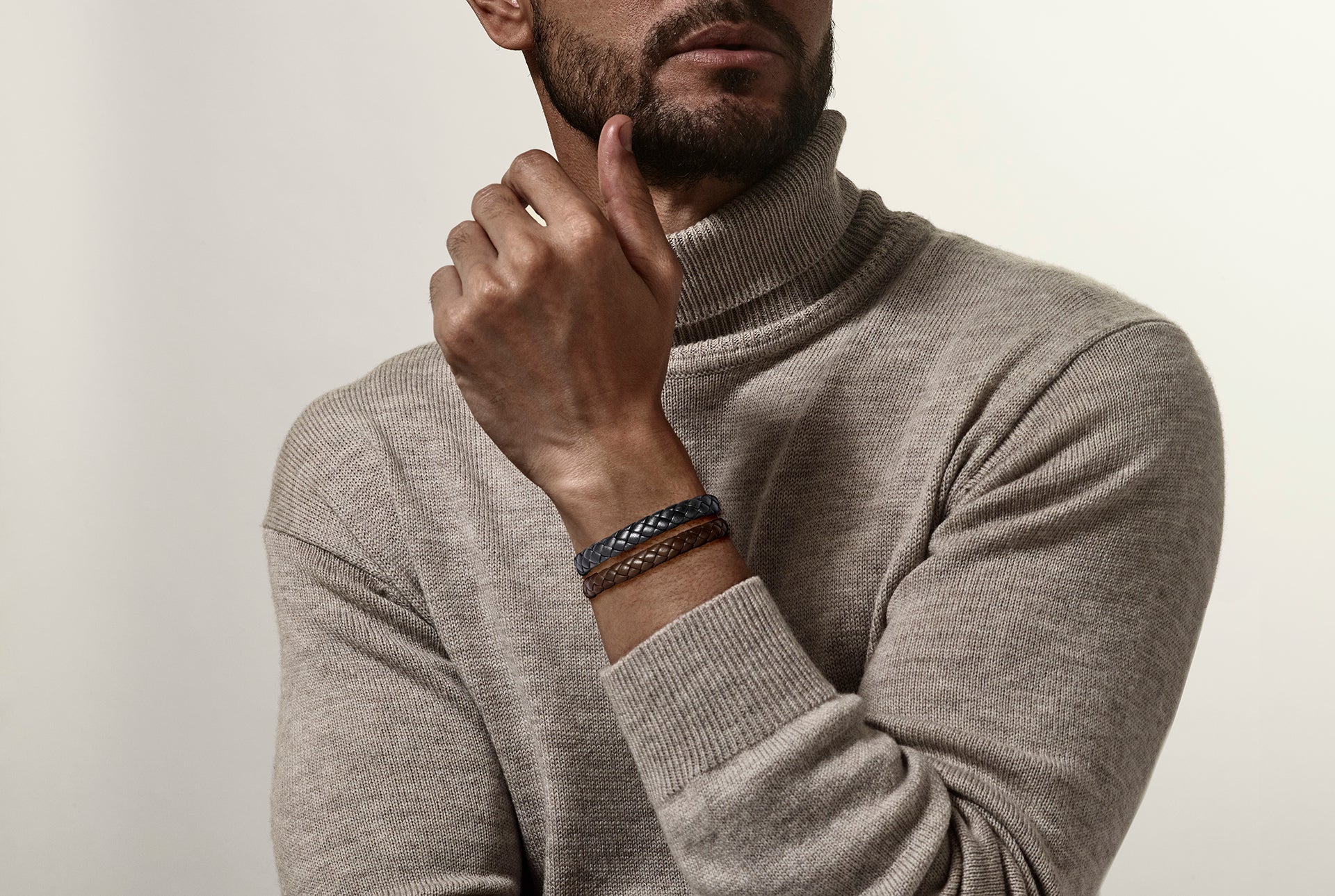 Black wide braided leather bracelet with black steel slide clasp worn on man's wrist with beige turtleneck