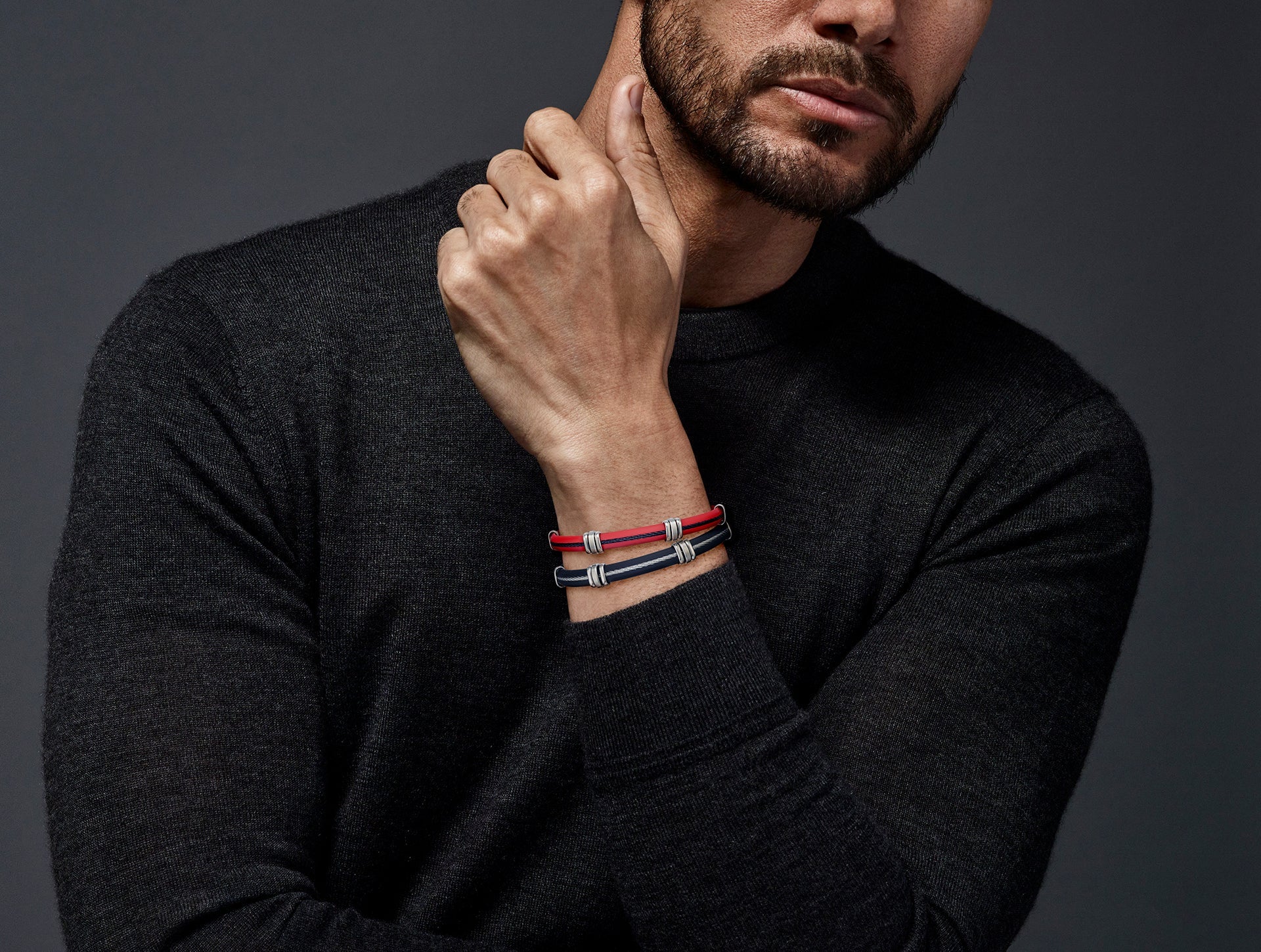Man in dark grey turtleneck stacking red and navy rubber steel cable ID bracelets — Jan Leslie