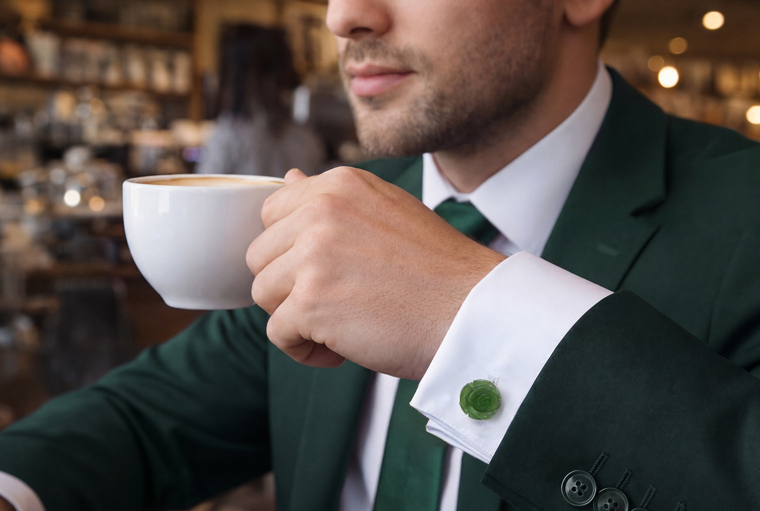 Man in forest green suit and green tie holding white coffee cup in café wearing hand-carved nephrite jade rose cufflink on white French cuff dress shirt, Jan Leslie 