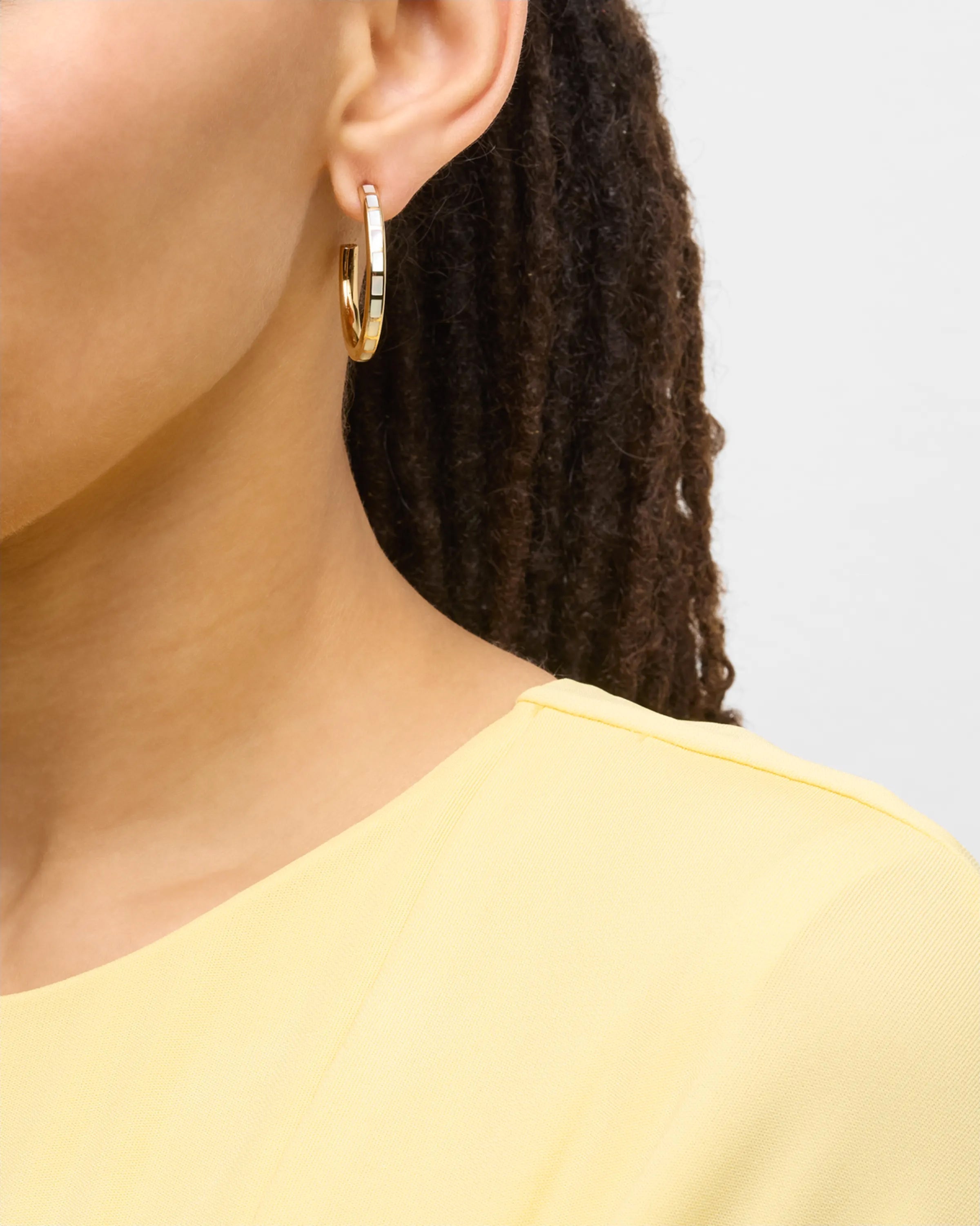 Model in yellow top wearing small gold hoop earrings with multicolor enamel tile inlays — Jan Leslie