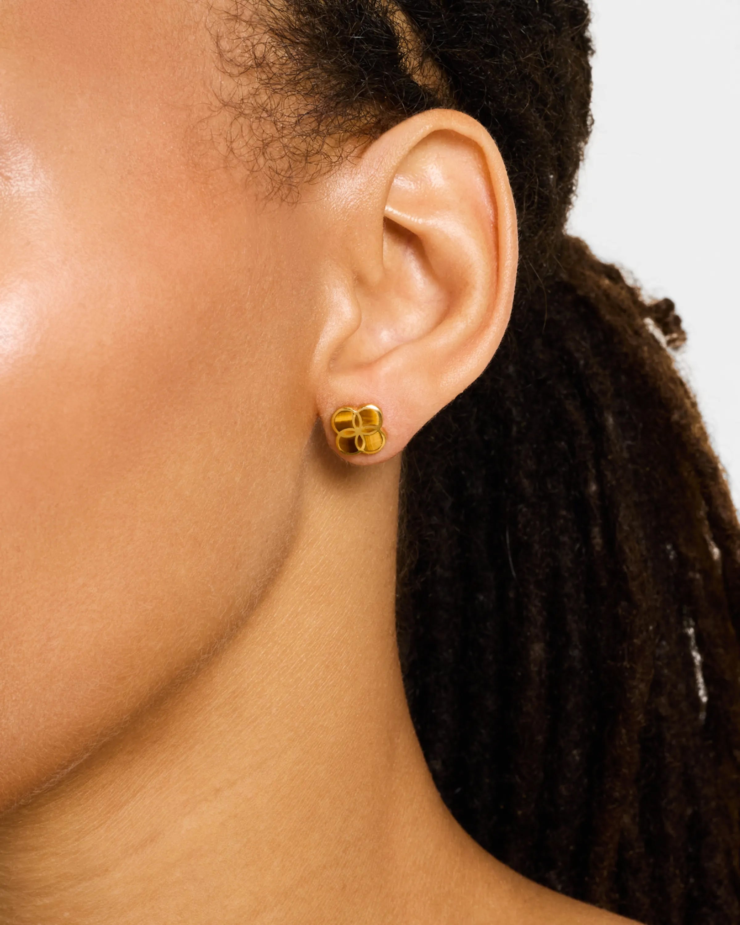Woman wearing solid gold quatrefoil clover stud earrings with high-polish domed finish, luxury minimalist women's fine jewelry lifestyle.