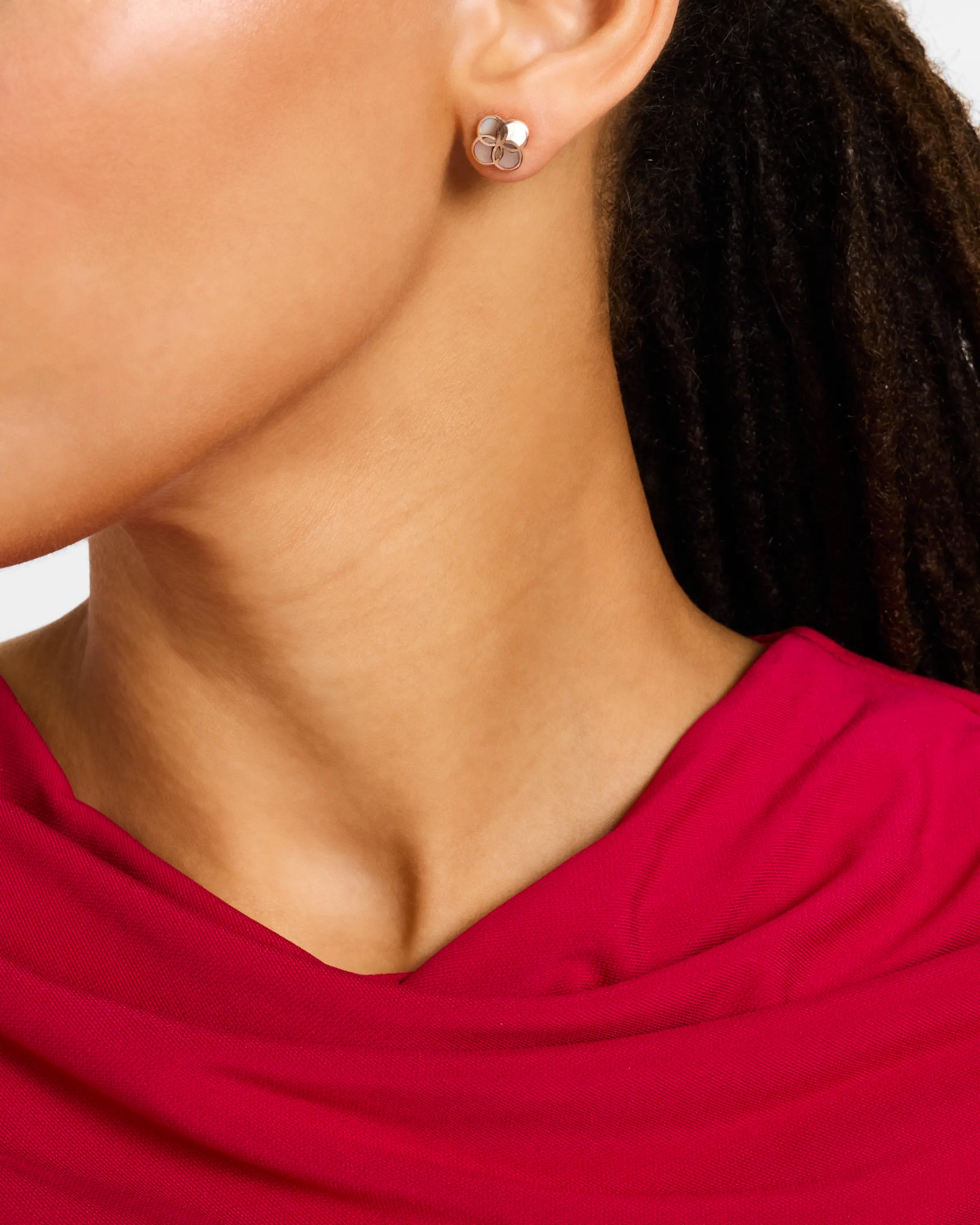 Woman in deep crimson dress wearing 18K gold vermeil sculptural petal clover stud earring at lobe showing four raised convex domed polished gold lobes by Jan Leslie