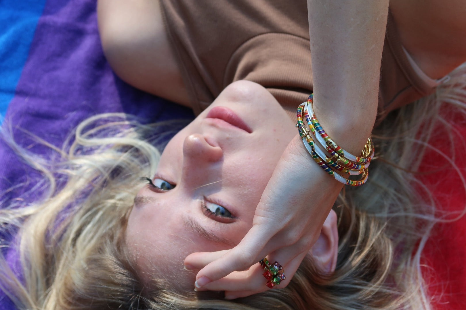 Model is wearing Jan Leslie's SINGLE Rainbow Gummy Bear Sterling Silver Ring with 18K Gold Vermeil and three Stripe Gemstone & Enamel Sterling Silver Stackable Bangle Bracelets in rainbow on gold. 
