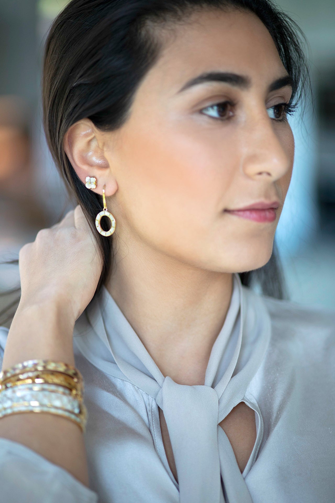 Woman wearing gold quatrefoil mother of pearl stud earrings with matching black onyx oval drop earings.