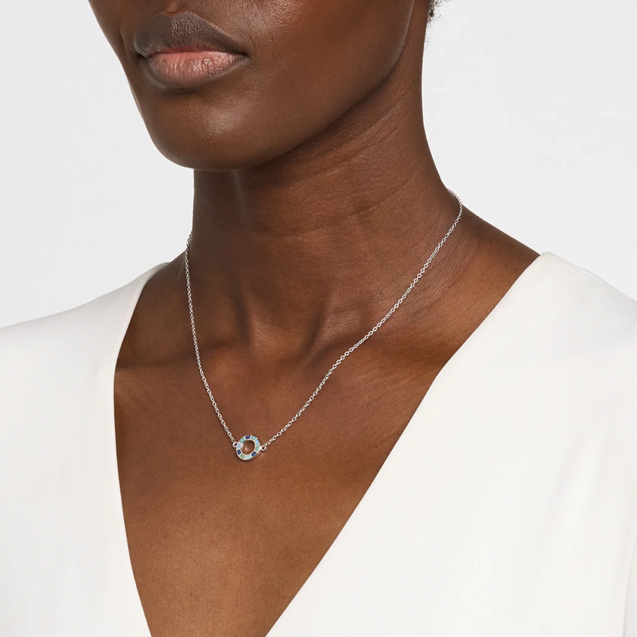 Woman in white v-neck top wearing a sterling silver pendant necklace with a single open circle blue and teal enamel mosaic pendant.