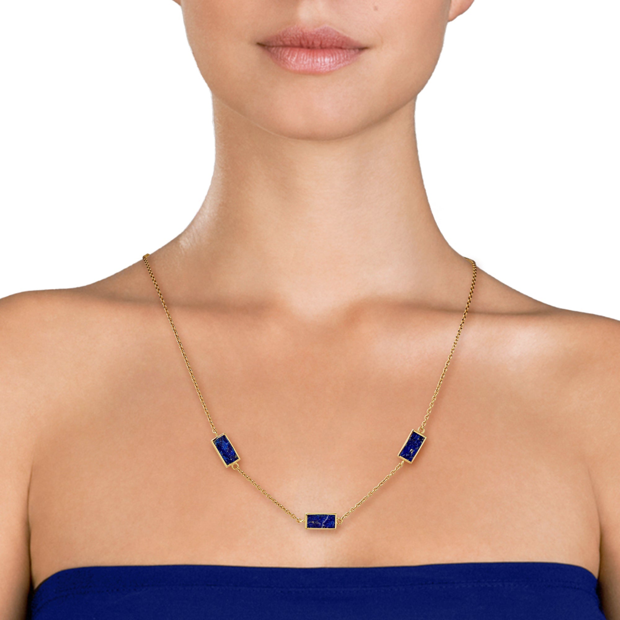Woman in cobalt blue strapless dress wearing a gold cable chain station necklace with three rectangular lapis lazuli stone pendants in gold bezel settings.