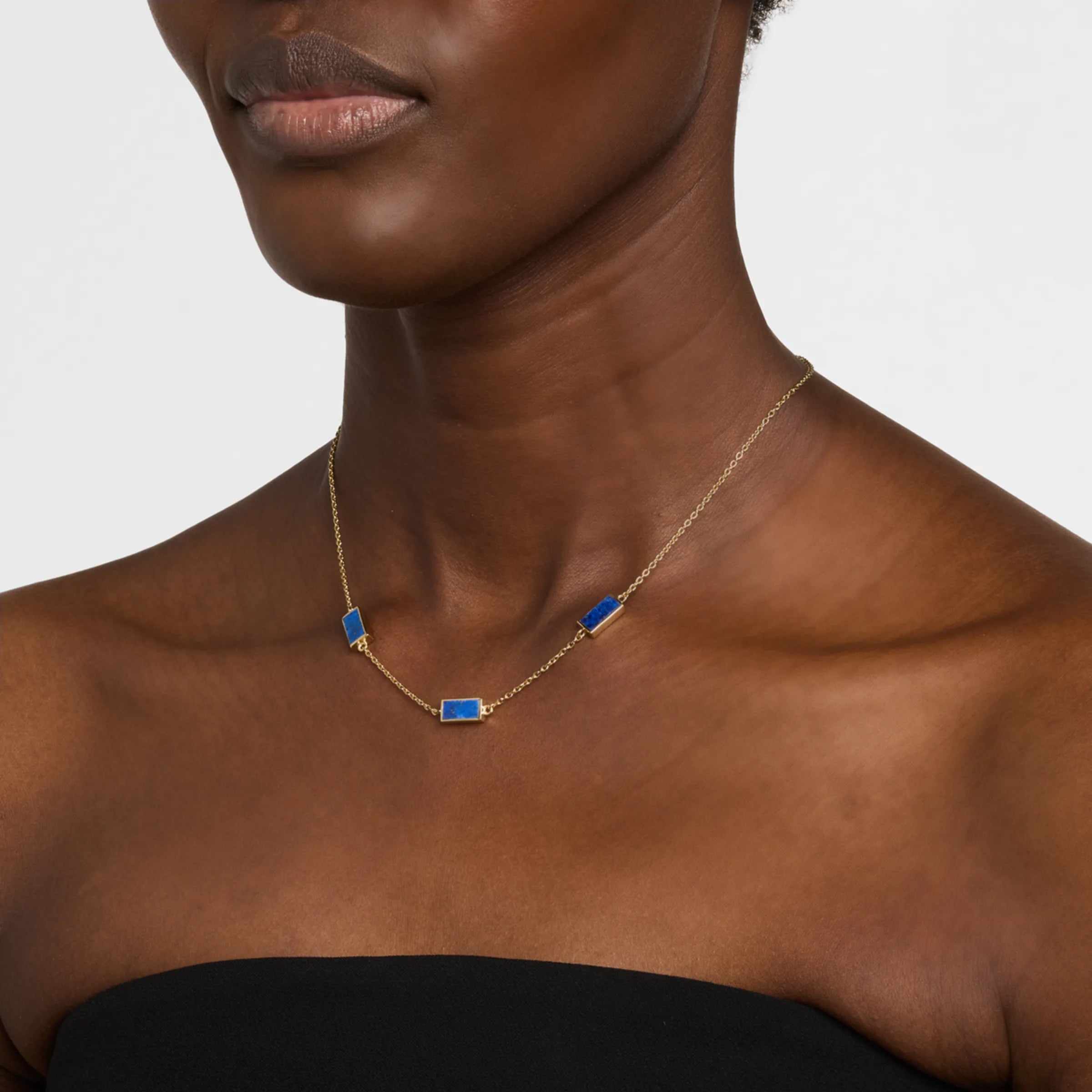 Woman in black strapless top wearing a gold cable chain station necklace with three rectangular lapis lazuli stone pendants.