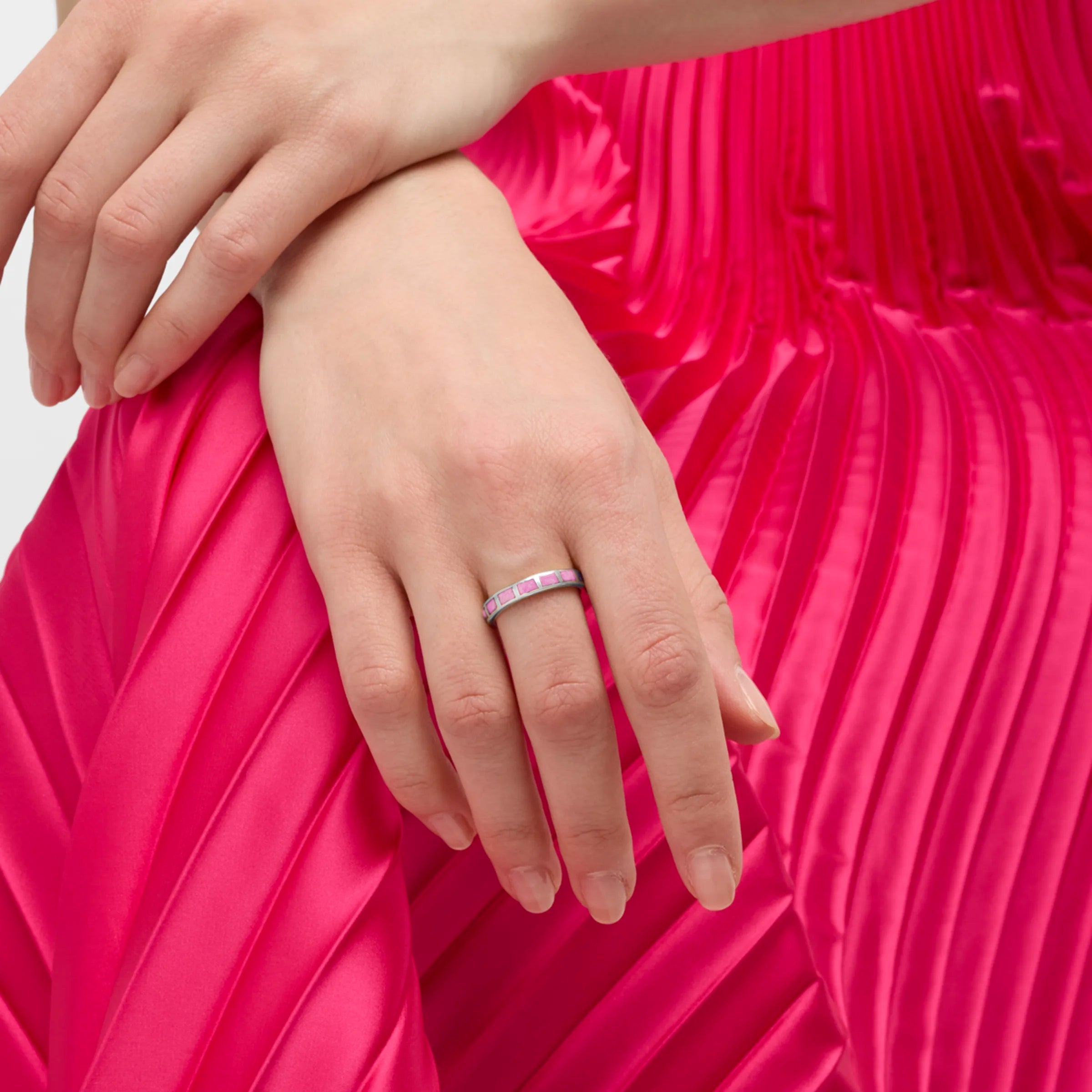 Woman wearing sterling silver segmented pink enamel eternity band ring on middle finger against hot pink pleated satin skirt, Jan Leslie luxury women's fine jewelry lifestyle.