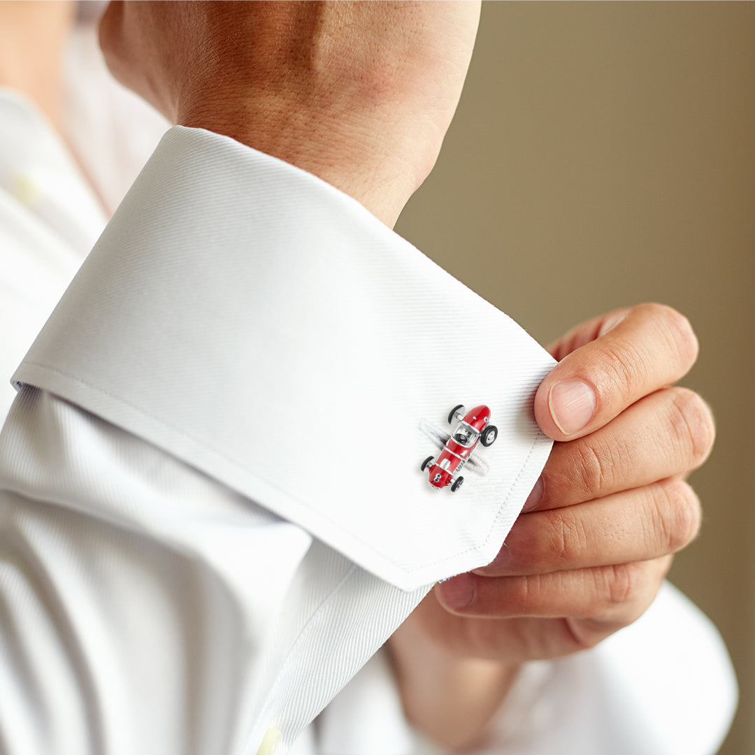 Man wearing 3D red enamel vintage Formula One racing car cufflink on white French cuff, close-up wrist detail, luxury motorsport men's fine jewelry lifestyle.