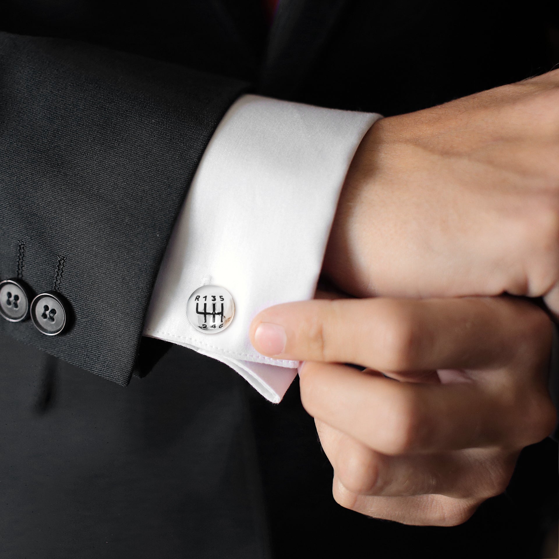 Man fastening sterling silver gear shift knob cufflinks on white French cuff with black suit.