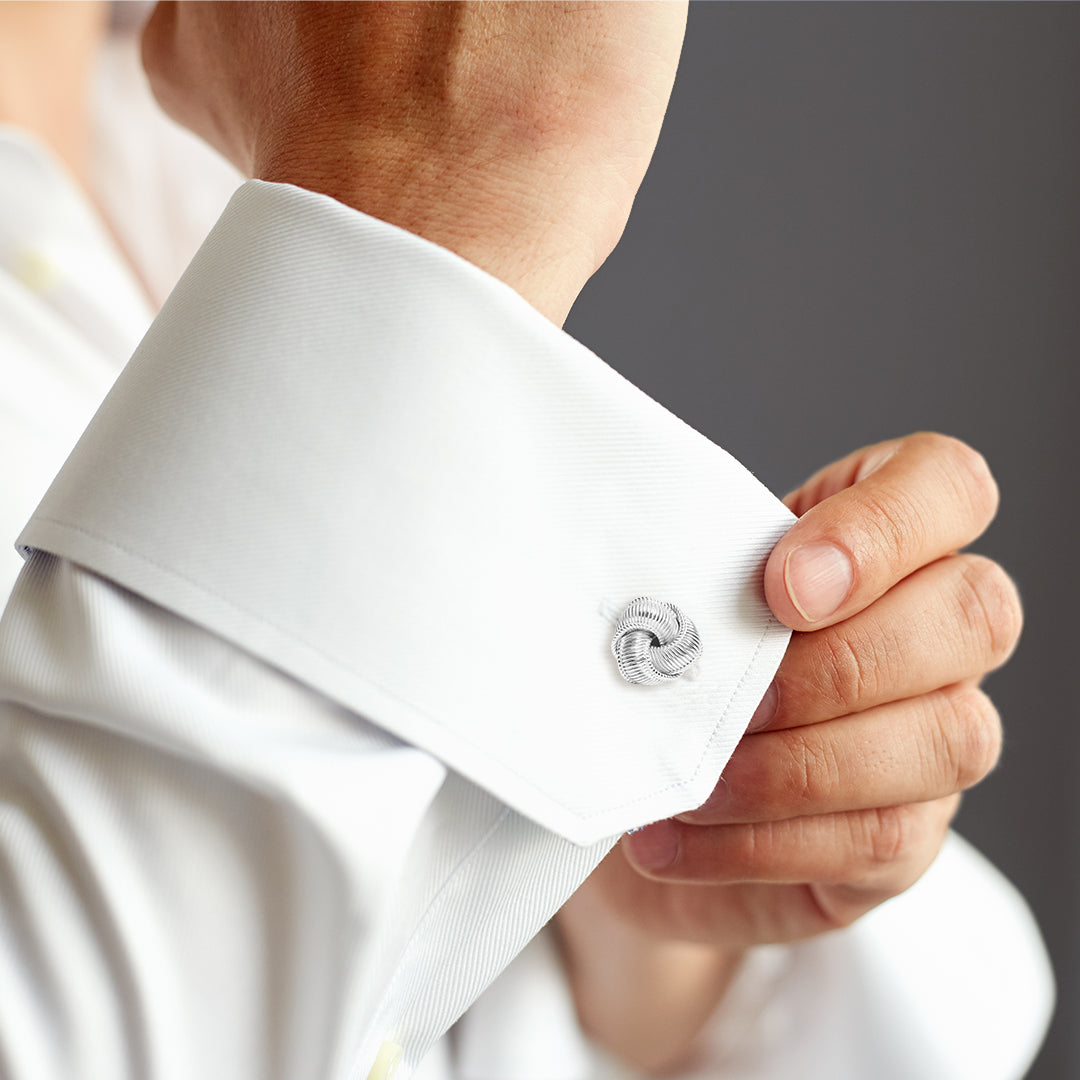Man fastening sterling silver ribbed love knot cufflinks on white French cuff shirt.
