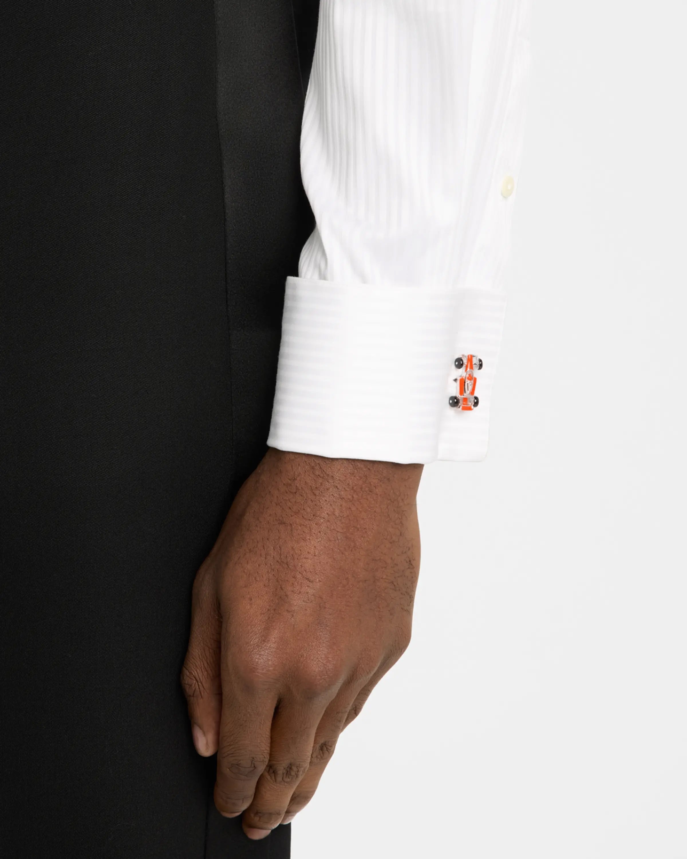 Man in black tuxedo jacket and white pleated bib dress shirt wearing sterling silver and orange enamel Formula 1 racing car cufflink on cuff, Jan Leslie